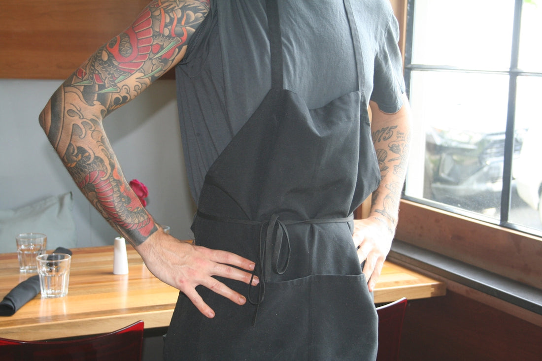 Person with tattoos wearing a black apron